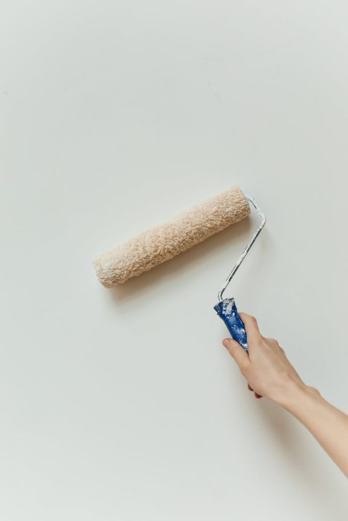 A hand applying paint on a wall using a roller brush; minimalistic home renovation scene.