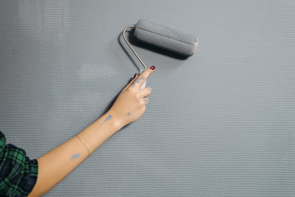 person-painting-wall-with-paint-roller-6764289 A close-up of a persons hand using a paint roller on a blue wall for home renovation.