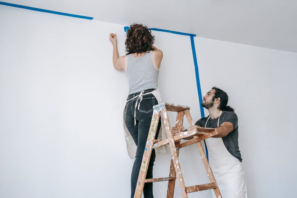 woman-on-a-stepladder-painting-a-wall-7217989 A couple collaborates on home renovation with paint and ladder.